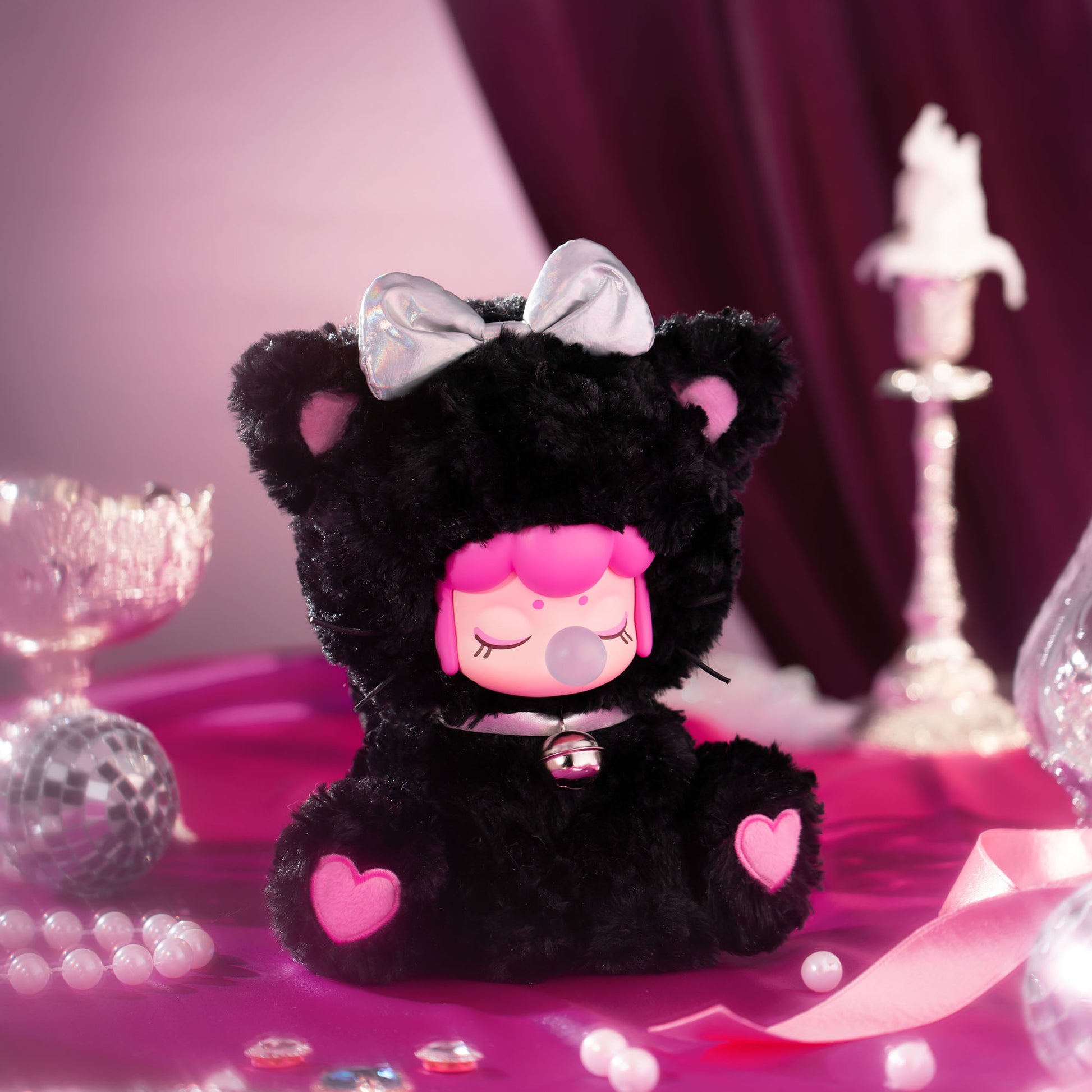 Black plush toy with pink accents and a bow on a decorative background