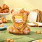 Plush toy resembling a cat with a pumpkin on its head, surrounded by bread and pastries.