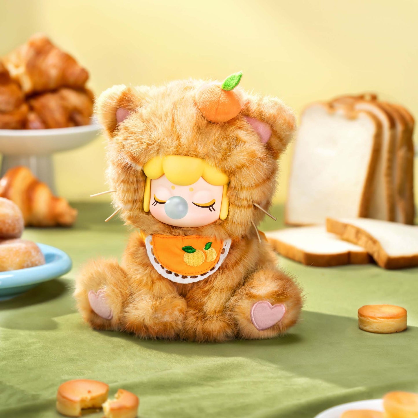 Plush toy resembling a cat with a pumpkin on its head, surrounded by bread and pastries.