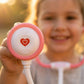 Child holding a pink and white toy stethoscope with a heart design, outdoors.
