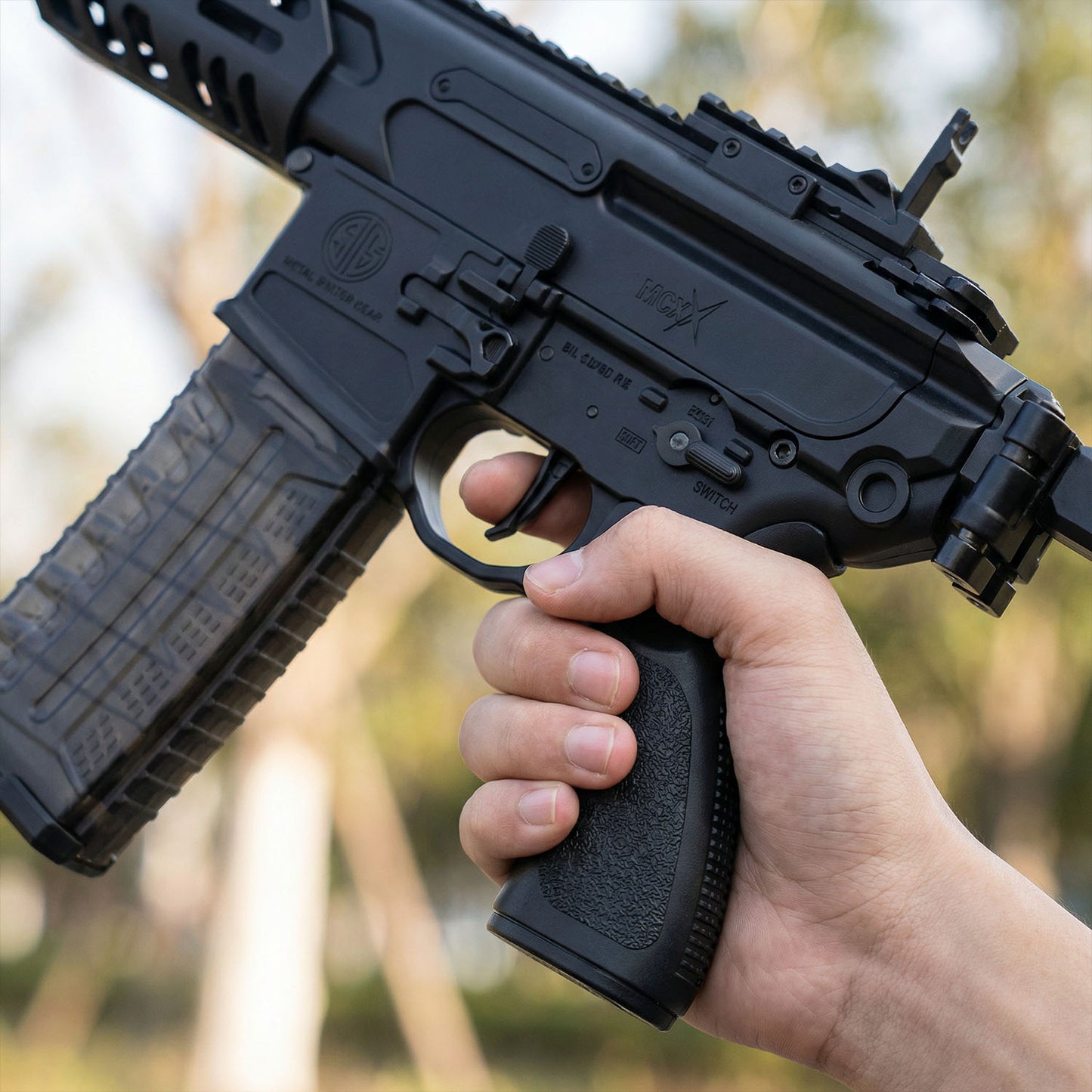 Hand holding a black rifle with a blurred natural background