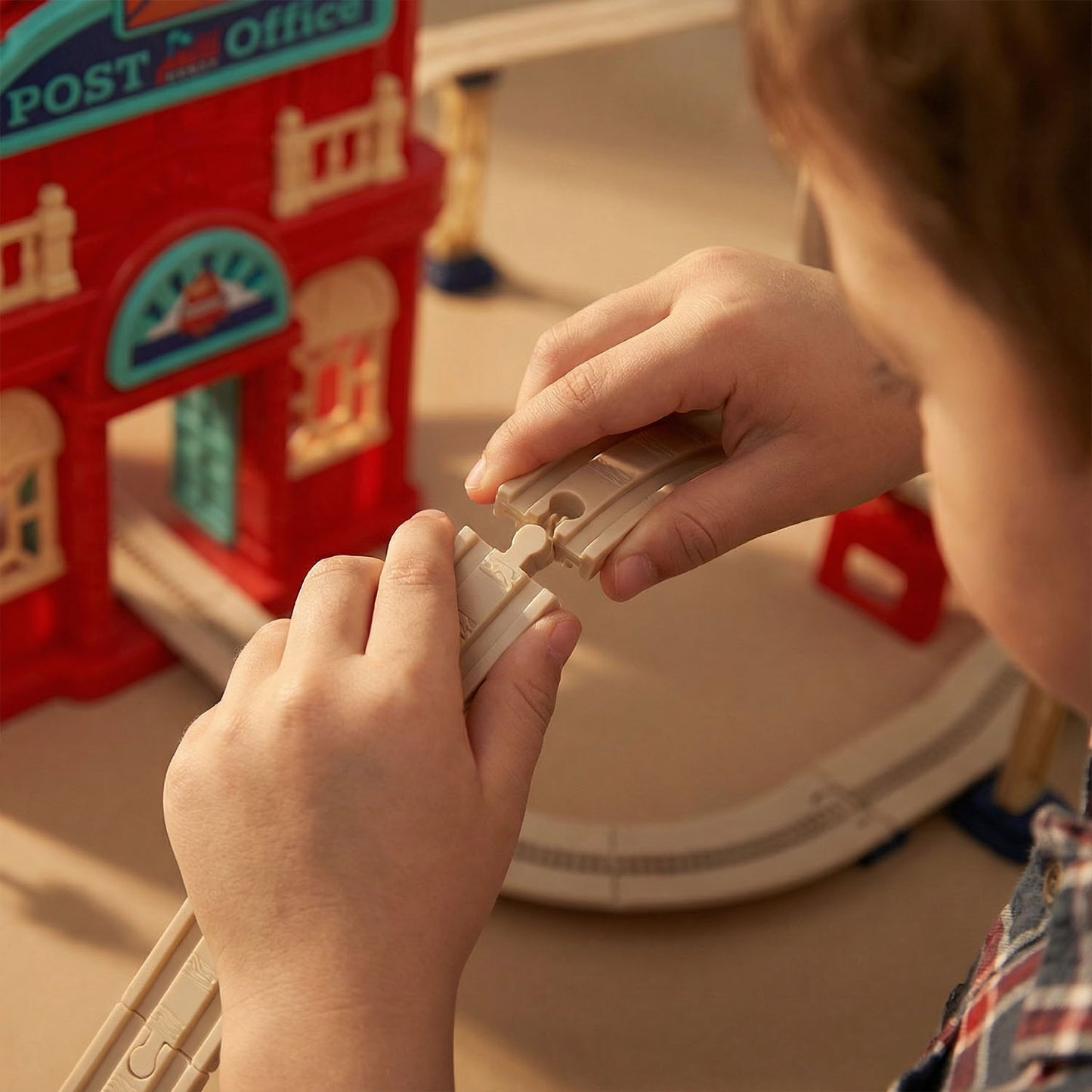 Child playing with a toy train set in front of a toy post office.